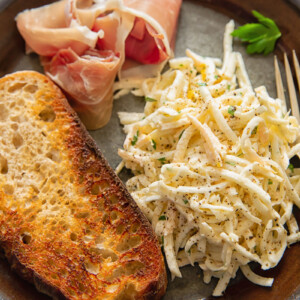 top down view of brown plate with celeriac remoulade, toasted bread slice and Parma ham slice