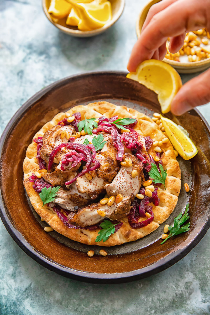 Person squeezing lemon over Chicken Musakhan on flatbread