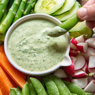 sugar snap pea is being dipped into a green goddess sauce