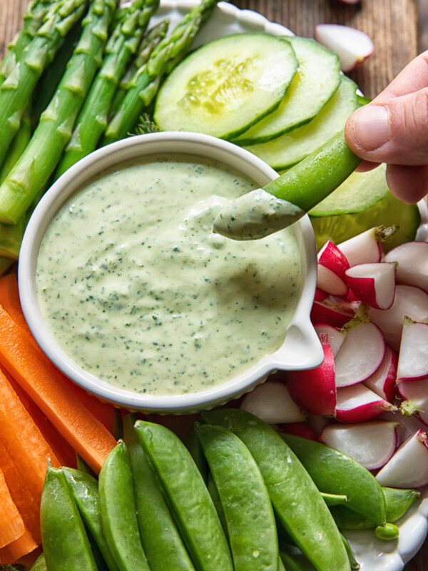 sugar snap pea is being dipped into a green goddess sauce
