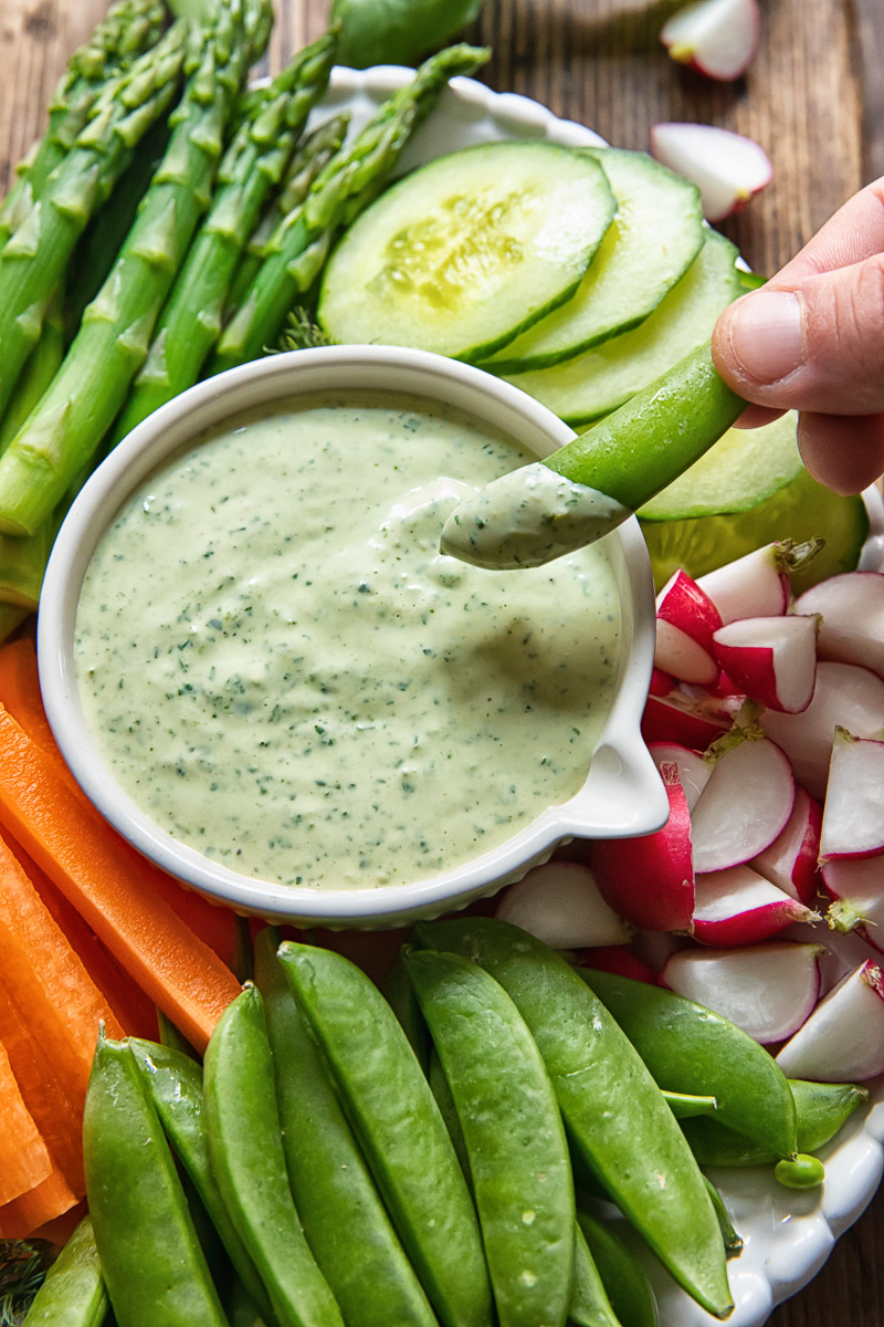 sugar snap pea is being dipped into a green goddess sauce