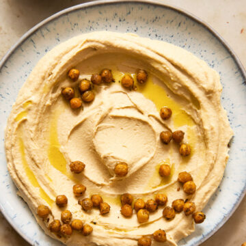 top down view of hummus spread on a light blue plate, topped with chickpeas and olive oil