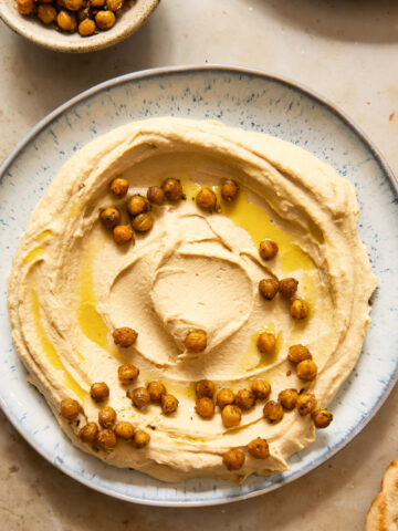 top down view of hummus spread on a light blue plate, topped with chickpeas and olive oil