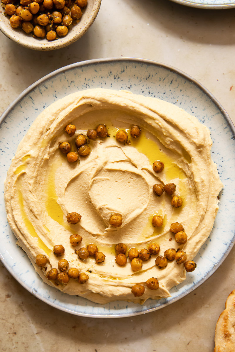 top down view of hummus spread on a light blue plate, topped with chickpeas and olive oil