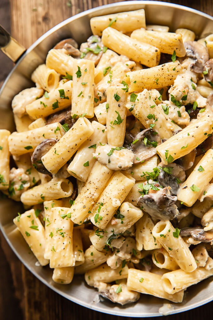 top down view of pan filled with creamy pasta, chunks of chicken sausage and sliced mushrooms.