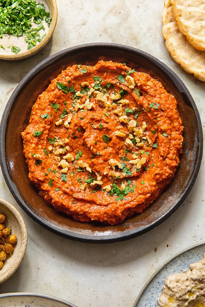 Top down view of Muhammara dip in bowl sprinkled with walnuts and parsley