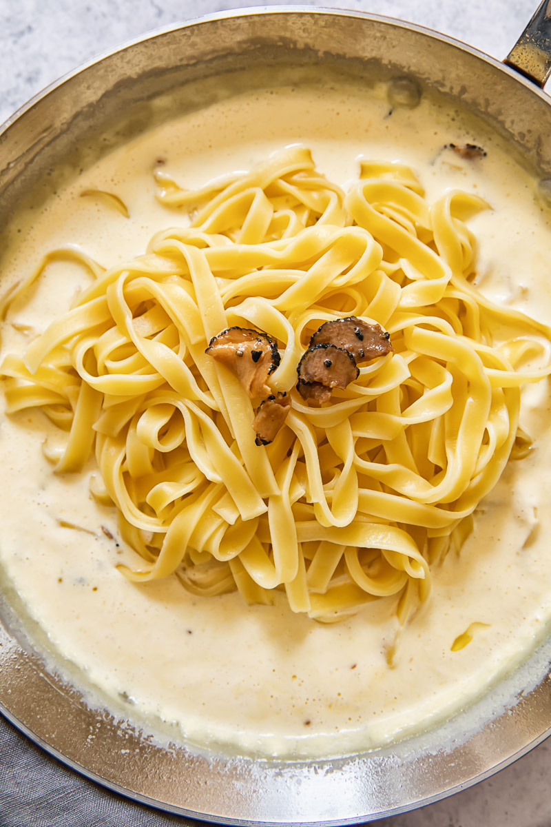 Process shot of tagliatelle pasta being added to truffle sauce in pan