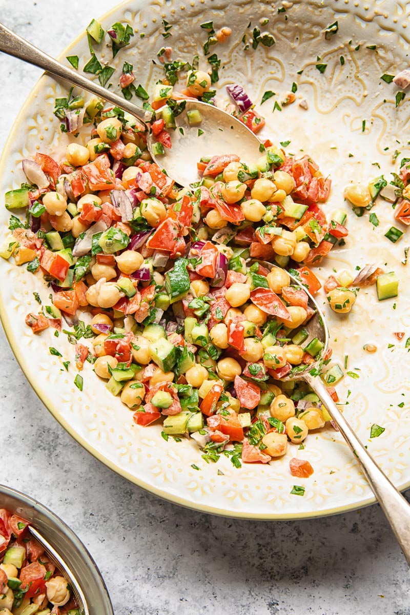 chopped salad with chickpeas in a salad bowl with two serving spoons