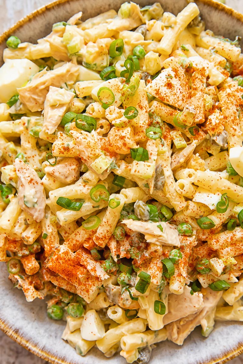 Close up of tuna macaroni salad with peas and green onion in a bowl.