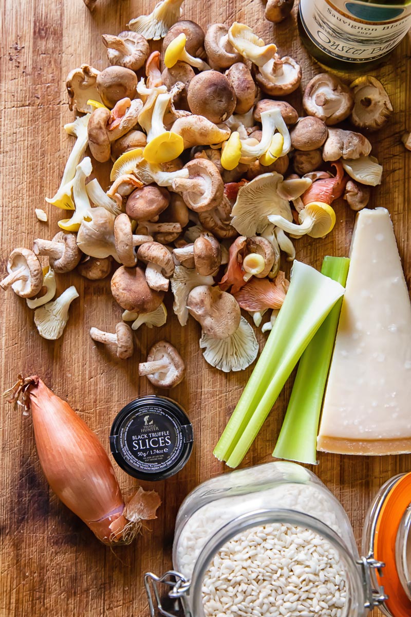 top dow view of wild mushrooms, a shallot, 2 celery sticks, a wedge of Parmesan and truffles in a small jar