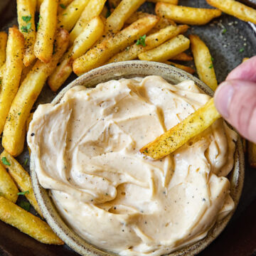 Top down shot of person dipping a fry into truffle aioli dip.