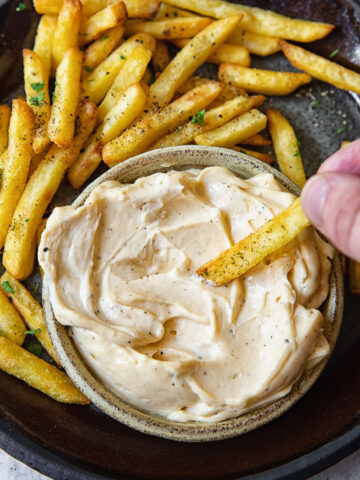 Top down shot of person dipping a fry into truffle aioli dip.