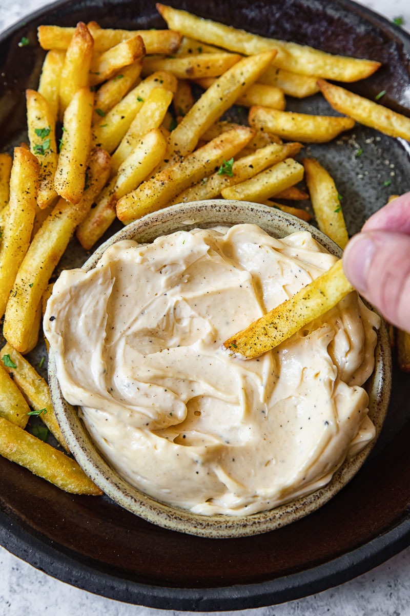 Top down shot of person dipping a fry into truffle aioli dip.