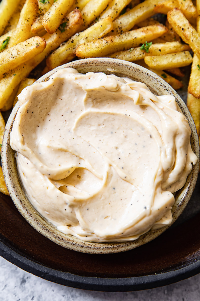 Close up shot of truffle aioli in a bowl next to fries.