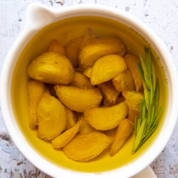 top down view of confit garlic cloves in oil in a white cup