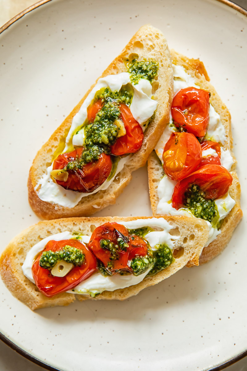 three slices of baguette topped with whipped ricotta and cherry tomatoes with pesto