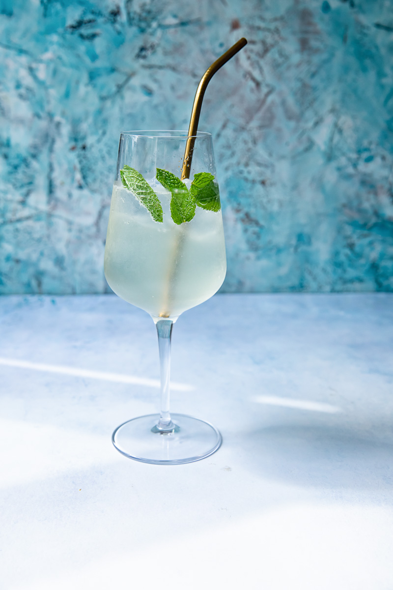 Side shot of Mojito spritz in a glass with a straw and mint.