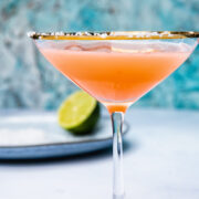 Side shot of blood orange margarita in a cocktail glass next to a lime