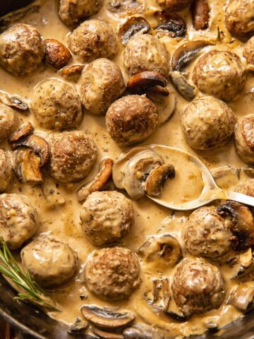 Top down view of spoon scooping meatballs in Marsala sauce from a pan