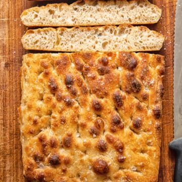 Top down view of focaccia slices next to loaf of sourdough focaccia on a cutting board
