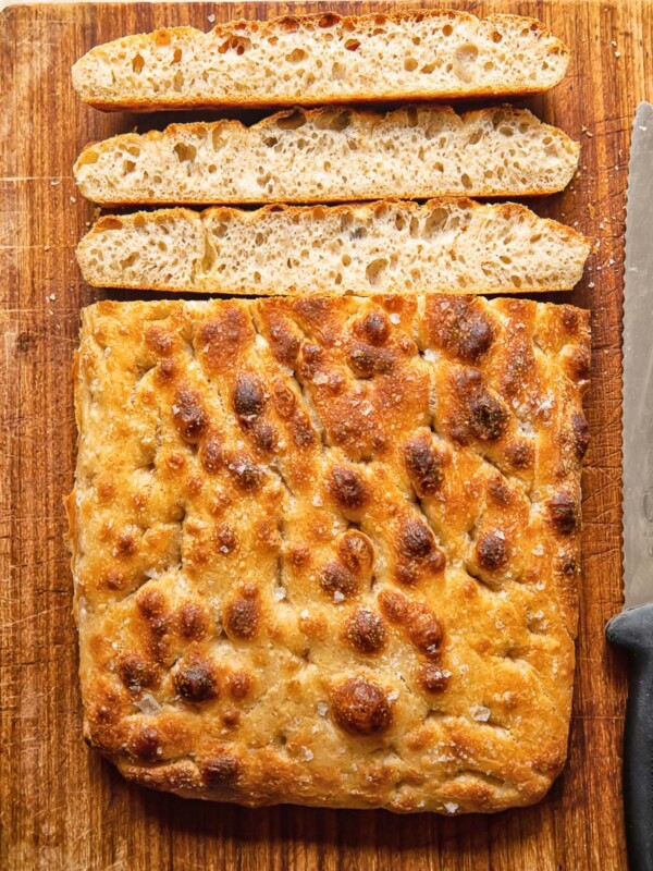 Top down view of focaccia slices next to loaf of sourdough focaccia on a cutting board