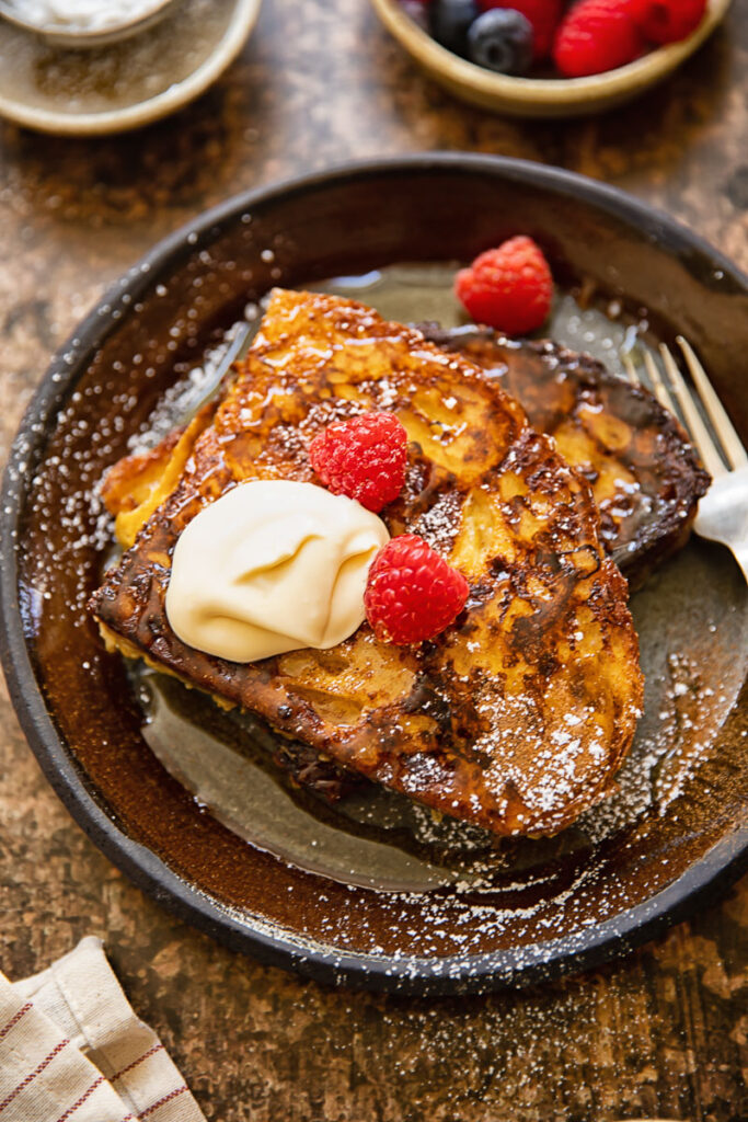 Top down shot of french toast with creme fraiche and raspberries on a plate