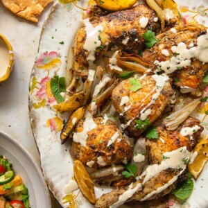 Top down view of tahini sauce drizzled over za'atar chicken with lemon and garlic on a platter