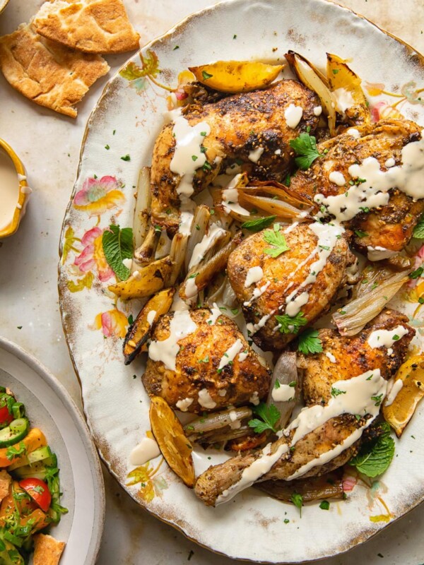 Top down view of tahini sauce drizzled over za'atar chicken with lemon and garlic on a platter