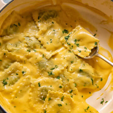 spoon holding a parcel of ravioli in pot of pasta in squash sauce