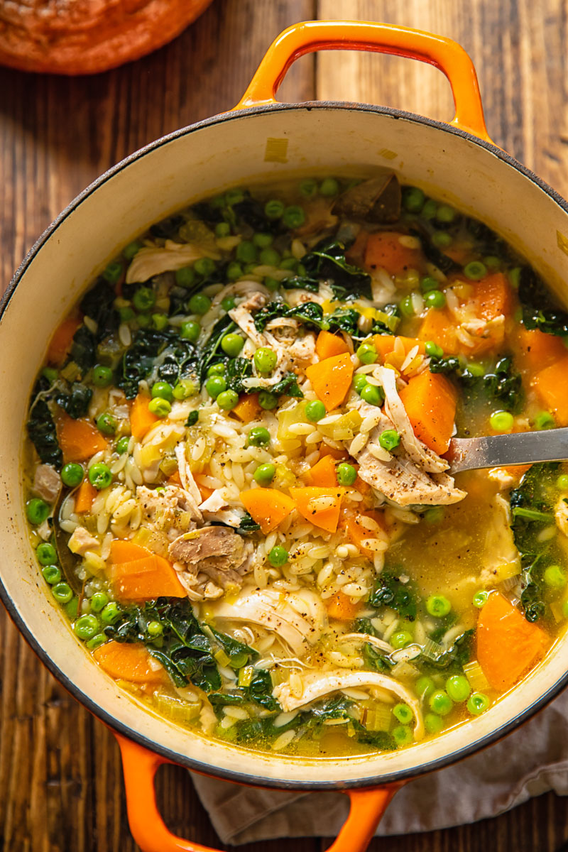 Top down view of chicken vegetable soup with orzo being scooped out of a pot