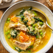 Top down view of chicken and vegetable soup with orzo, carrots and peas in a bowl with a spoon