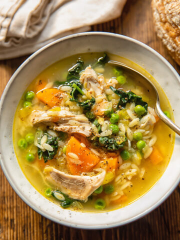 Top down view of chicken and vegetable soup with orzo, carrots and peas in a bowl with a spoon