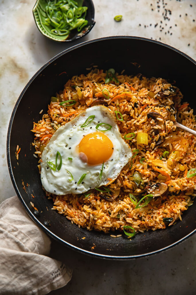 Wok with kimchi fried rice and a fried egg next to a small dish of sliced green onions