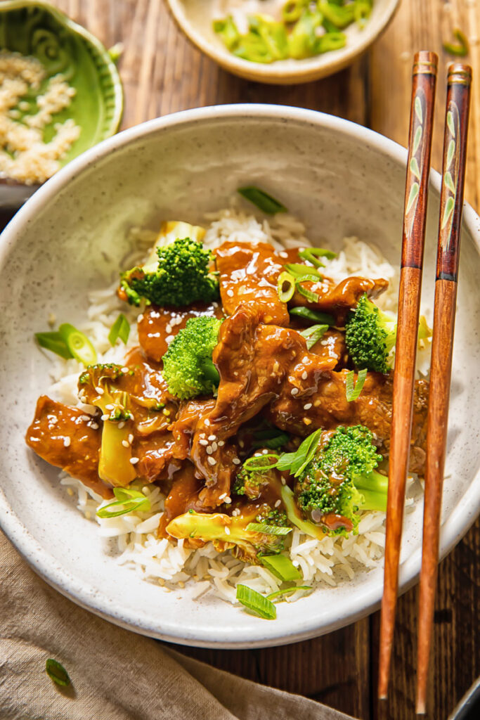 bowl of beef and broccoli stir fry with chop sticks