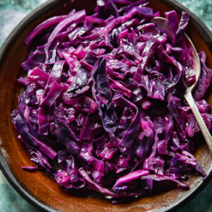 Top down view of braised red cabbage on a plate with bacon lardons and juniper berries