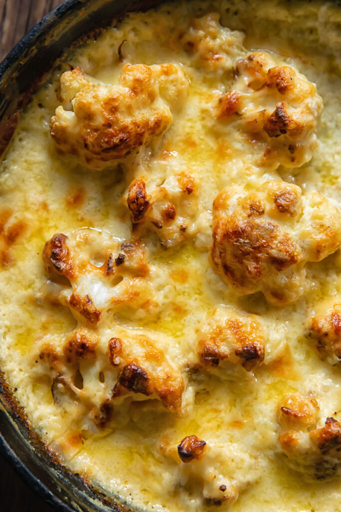 Top down view of cauli florets in a pan covered in cheesy Mornay sauce