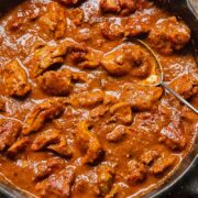 close up of a pan of chicken rogan josh with a serving spoon