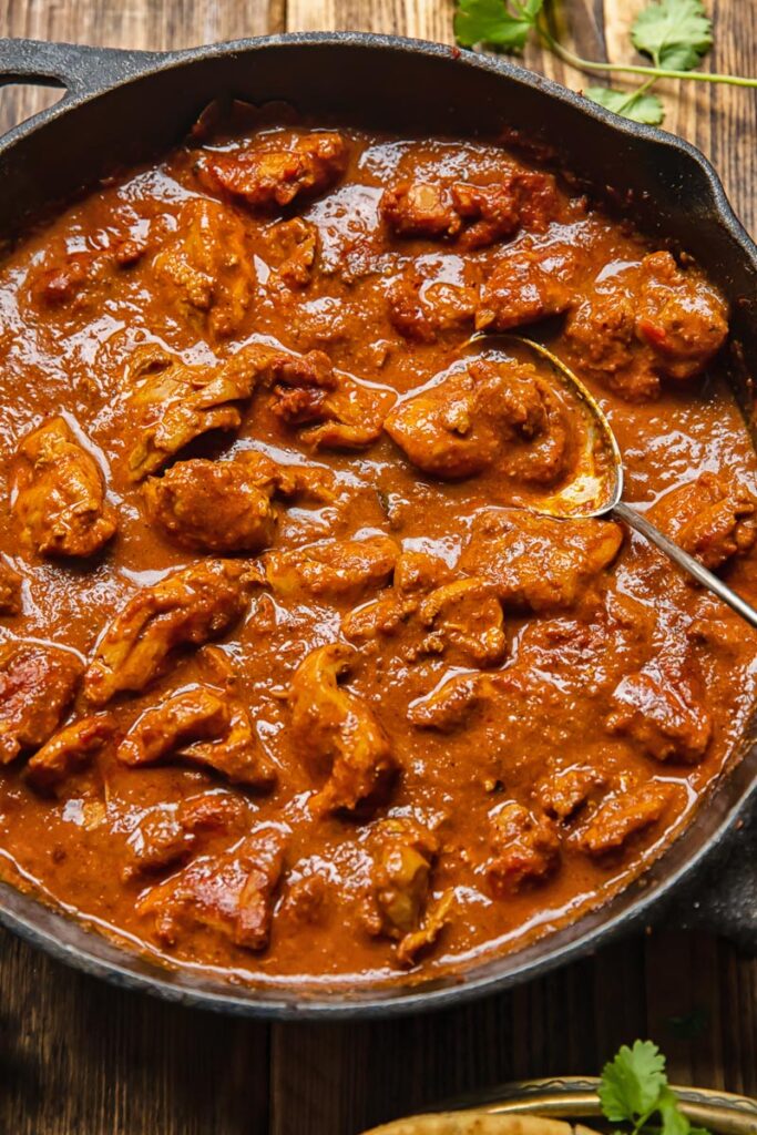 close up of a pan of chicken rogan josh with a serving spoon