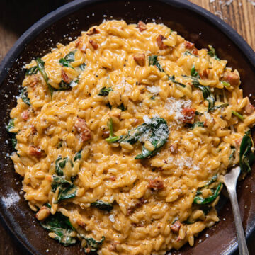 Top down view of creamy orzo with chorizo and spinach on a plate with a fork