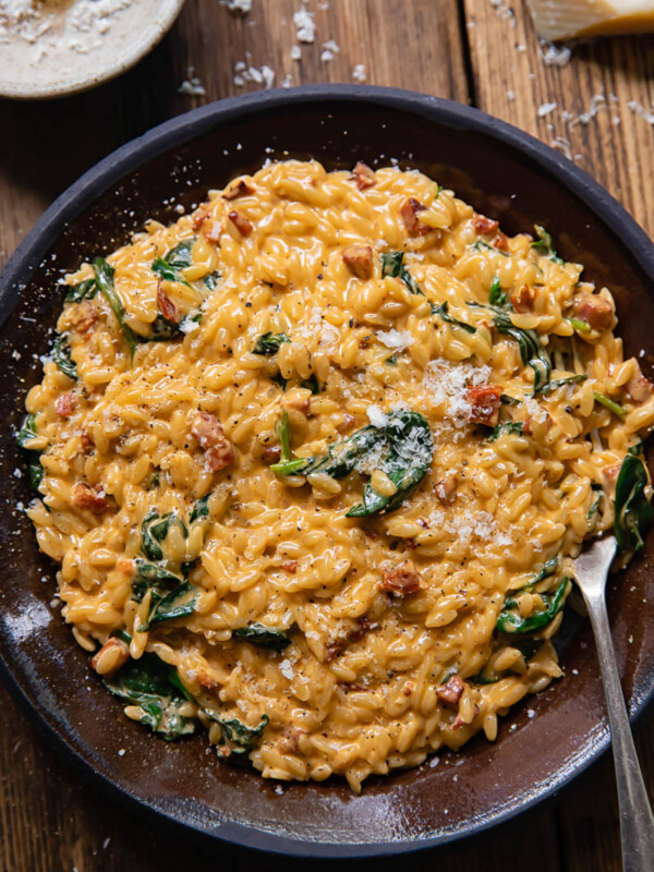 Top down view of creamy orzo with chorizo and spinach on a plate with a fork