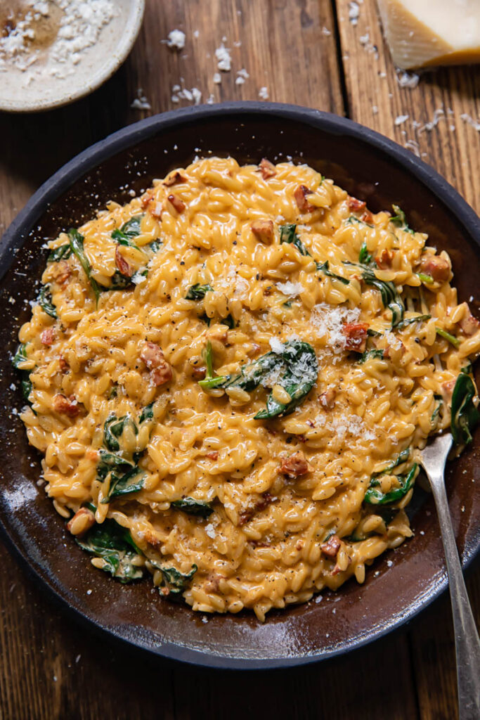 Top down view of creamy orzo with chorizo and spinach on a plate with a fork