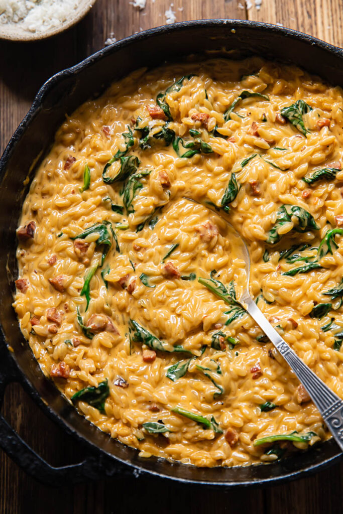 Top down shot of spoon scooping orzo with chorizo and spinach out of a pan