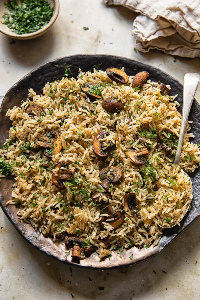 Top down view of rice cooked with garlic and mushrooms with dill and parsley on a plate