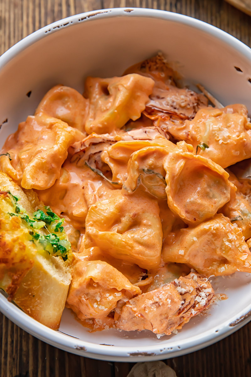 bowl of tortellini in cream sauce with piece of garlic bread