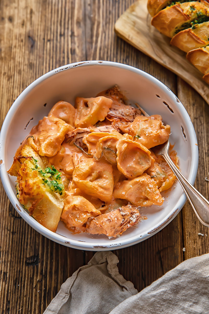 bowl of tortellini with a fork and garlic bread