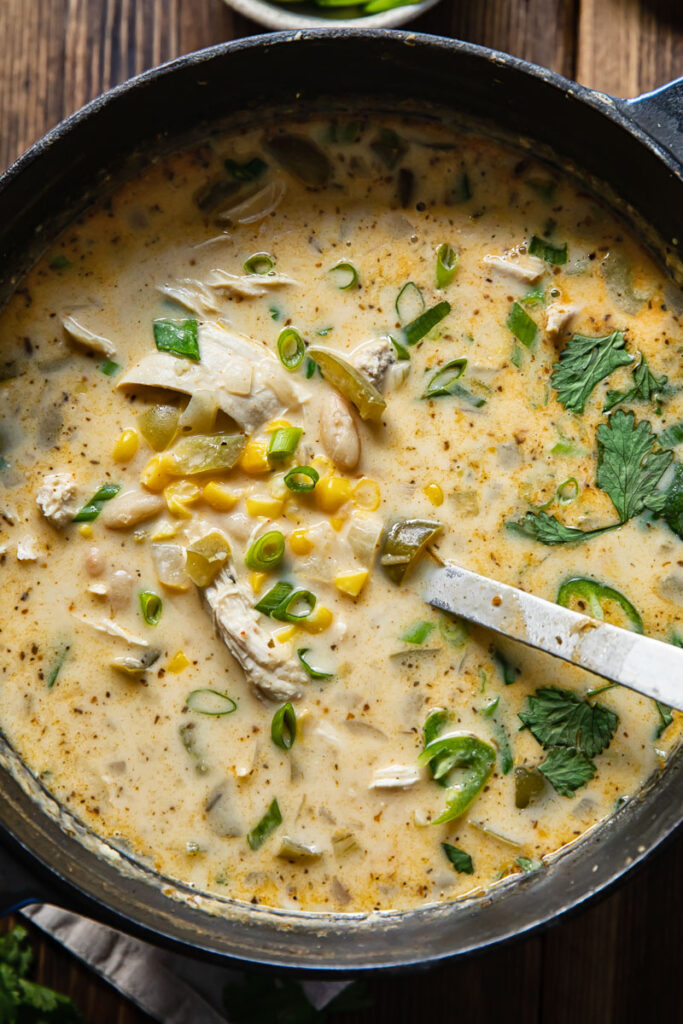 Close up shot of white chicken chili in a large pot with a ladel