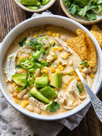 Top down view of white chicken chili with corn, chillies and avocado in a bowl