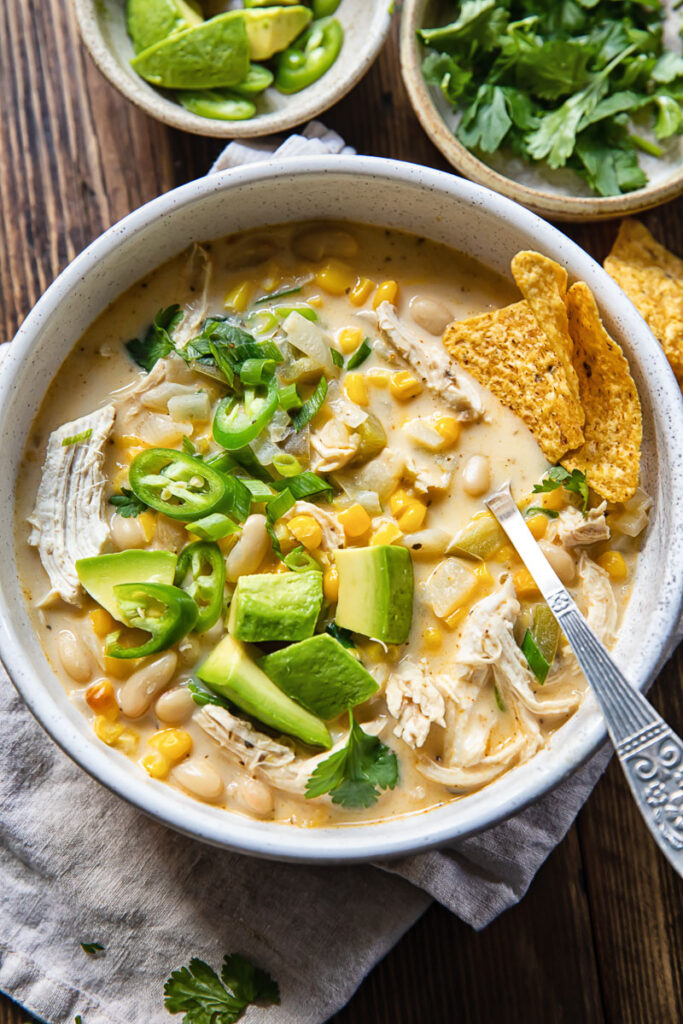 Top down view of white chicken chili with corn, chillies and avocado in a bowl