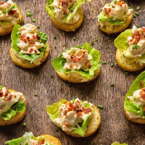 Close up shot of many chicken Caesar crostinis laid next to each other on a cutting board