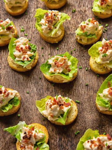 Close up shot of many chicken Caesar crostinis laid next to each other on a cutting board